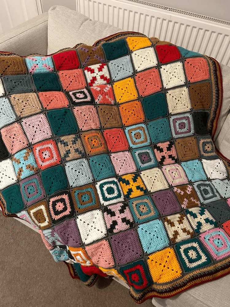A colourful handmade granny square crochet blanket draped over a sofa